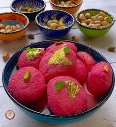 colorful desserts with gold leaf decorations in bowls on a white wooden table top, surrounded by nuts and other food items