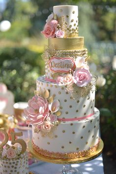 a three tiered wedding cake with pink flowers on top and gold trimmings