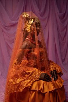 a woman dressed in an orange wedding gown and veil is standing next to a purple curtain