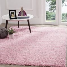 a living room with pink rugs and pictures on the wall, coffee table and potted plant