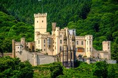 an old castle sits on top of a hill surrounded by green trees and hills in the background