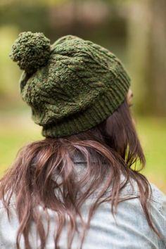 a woman with long hair wearing a green knitted pom - pom hat