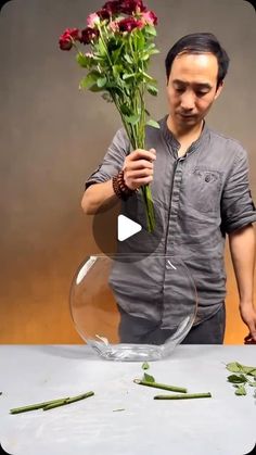 a man holding flowers in front of a glass bowl with stems sticking out of it