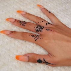 a woman's hand with tattoos on it and an orange manicured nail polish