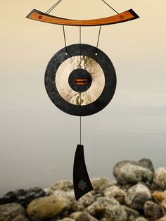 a wind chime hanging from the side of a body of water with rocks in front of it