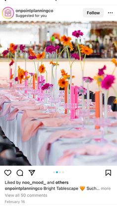 the table is set with pink and orange flowers in tall vases on each side