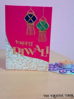 a pink card with two tassels on it and a candle next to it