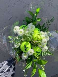 a bouquet of flowers with tennis balls and greenery on the side of a building