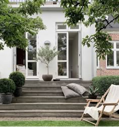 a white house with steps leading to the front door and sitting area on the lawn