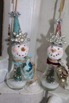 two snowmen are sitting on top of glass bottles with ornaments hanging from the sides