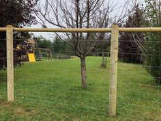 a fenced in play area with a tree and swing set on the other side