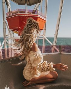 a woman sitting on the edge of a boat looking out at the ocean and her hair blowing in the wind