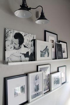 some pictures are hanging on the wall above a shelf with lights and framed photos in it