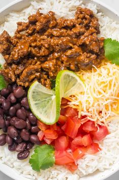 a white bowl filled with rice, beans, and other foods including limes on the side