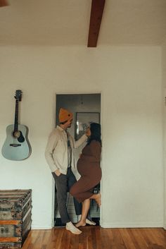 a man standing next to a woman in front of a door with a guitar hanging on the wall