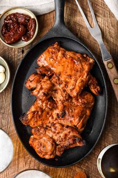 some meat is cooking in a skillet on a table with sauces and spoons