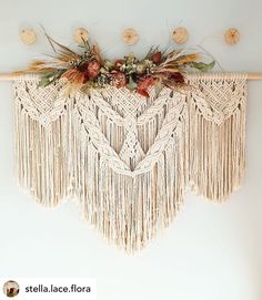 a macrame wall hanging with dried flowers and leaves on it's side