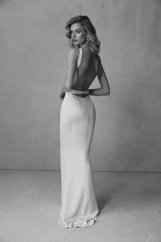 a woman in a long white dress posing for a black and white photo with her back to the camera