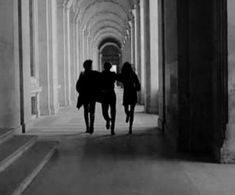 two people walking down a long hallway in black and white