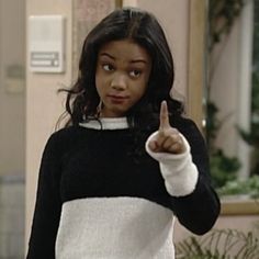 a woman in a black and white sweater pointing to the side with her finger up