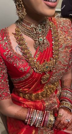 a woman in a red and gold bridal outfit with jewelry on her neck, smiling at the camera