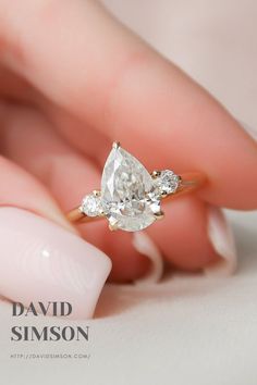 a woman's hand holding an engagement ring with two pear shaped diamonds