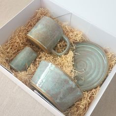 four tea cups and saucers in a box with some straw on the floor next to it