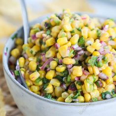 a bowl filled with corn and green onions on top of a wooden table next to a spoon