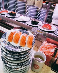 there are many sushi plates stacked on the counter next to cups and saucers