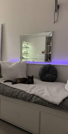 a black cat laying on top of a white bed next to a dresser and mirror