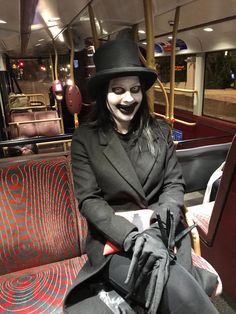 a man dressed up as the joker sitting on a train seat with his hat and gloves