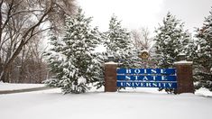 a blue and white sign sitting in the middle of a snow covered field next to trees