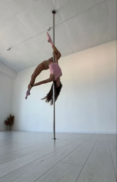 a woman is doing tricks on a pole in the middle of an empty room with white walls