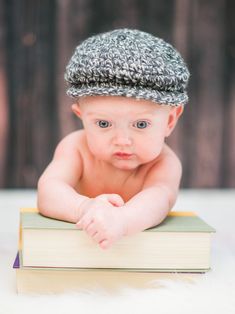 a baby laying on top of a book wearing a knitted hat and looking at the camera