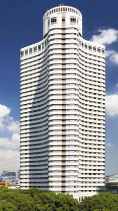 a tall white building sitting next to a lush green park filled with lots of trees