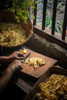 a person cutting up some food on a wooden board next to a potted plant