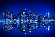 the city skyline is lit up at night and reflecting in the water with bright lights