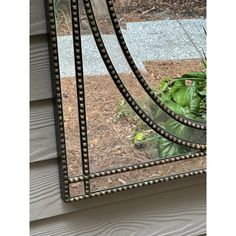 a mirror sitting on the side of a house next to a planter filled with flowers