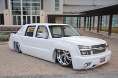 a white car parked in front of a building with large windows and chrome rims