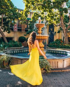 a woman in a yellow dress is standing near a fountain