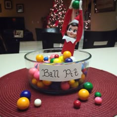 an elf is holding up a sign above a bowl full of candy balls with the word ball pit on it