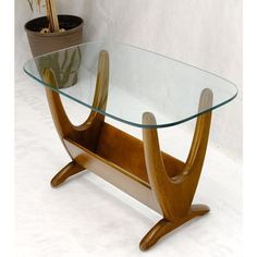 a glass table with wooden legs in front of a potted plant