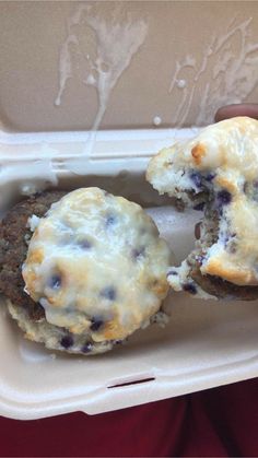 a person is holding up two blueberry muffins in a styrofoam container