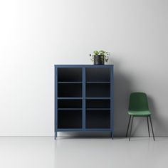 a green chair sitting next to a blue bookcase with plants on top and a white wall in the background