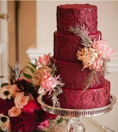 a red wedding cake sitting on top of a table next to a vase filled with flowers