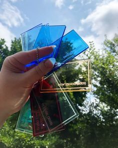 a person holding up four different colored business cards in their hand with trees in the background