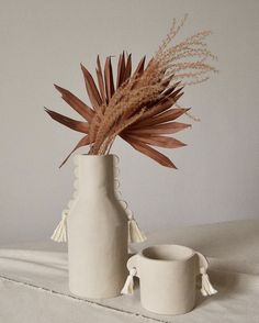 two white vases sitting on top of a bed next to each other with dried plants in them