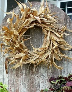 a wreath made out of dried corn on top of a wooden fence next to plants