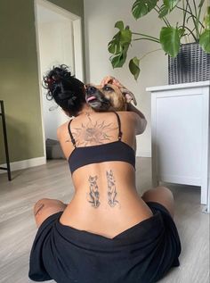 a woman sitting on the floor with her back turned to the camera while holding a dog