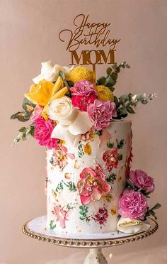 a birthday cake decorated with flowers and the words happy birthday mom on top is sitting on a pedestal